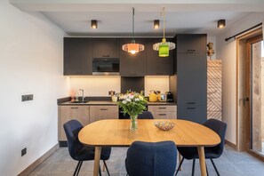 A modern kitchen with dark cabinetry, a wooden dining table, and pendant lights. - Solévivre – Terrace | Spa | View| Alpe d’Huez (Huez)
