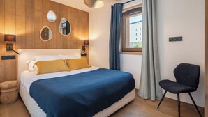 Quarto com cama, abajures, janela com cortinas e uma cadeira.
