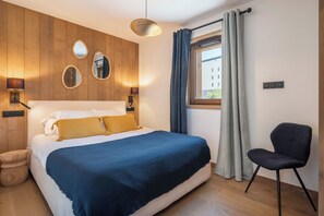 Un dormitorio con una cama, lámparas de noche, una ventana con cortinas y una silla.