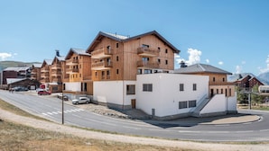 Um edifício de madeira com várias andares, varandas, fachada branca e uma estrada em primeiro plano.
