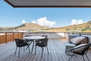 Una terraza al aire libre con una mesa y sillas, con vistas a un paisaje montañoso y edificios a lo lejos.