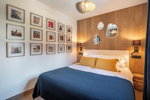 A bedroom with a bed, framed pictures on the wall, and a wooden panel design. - Solévivre – Terrace | Spa | View| Alpe d’Huez (Huez)