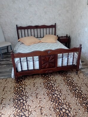 A bed with a wooden frame and a patterned bedspread, a small bedside table, and a chair. - Detached, single-story apartment in a completely quiet location, 500 meters from downtown (Lavelanet)