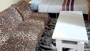 Une pièce avec un canapé à motifs léopard, un lit blanc recouvert d’une couverture à rayures et une table blanche.