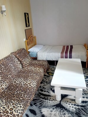 A room with a leopard print sofa, a white bed with a striped blanket, and a white table. - Detached, single-story apartment in a completely quiet location, 500 meters from downtown (Lavelanet)