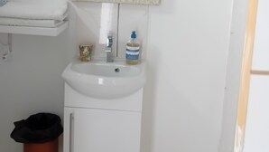 Une salle de bain avec un lavabo blanc, un miroir doté d’un cadre décoratif, une poubelle et des toilettes.