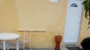 A small outdoor seating area with a table and chair, a potted plant, and a door.