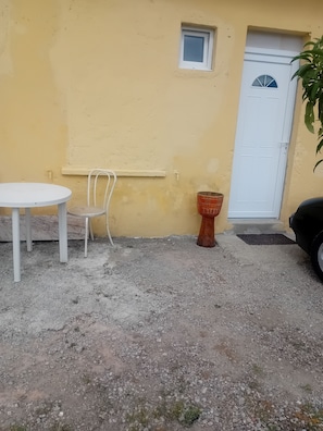 A small outdoor seating area with a table and chair, a potted plant, and a door.