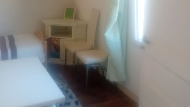 A room with a bed, a small table, a chair, and a desk with a chair. There is a window with curtains.
