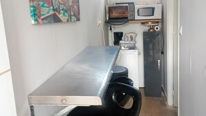 Une petite cuisine équipée d’un four à micro-ondes, d’une bouilloire et d’un petit réfrigérateur. On y trouve un tabouret de bar et une table avec un plateau en métal.