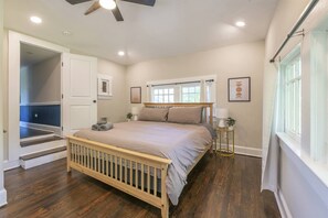 A bedroom with a wooden crib, a bed, a window with curtains, a nightstand, and a door leading to another room.