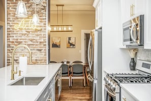 A modern kitchen with a brick wall, a neon sign, a dining area with chairs, and a stove. - Boho Home with driveway and lots of ensuite baths! (Atlanta)