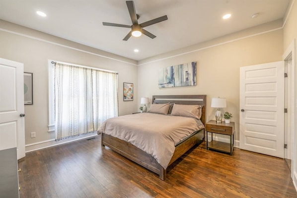 A bedroom with a bed, a ceiling fan, a nightstand, and a window with curtains.