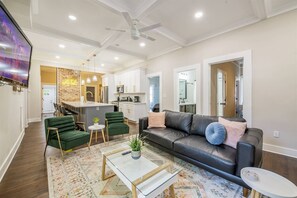 A modern living room with a leather sofa, green chairs, a coffee table, and a TV mounted on the wall.