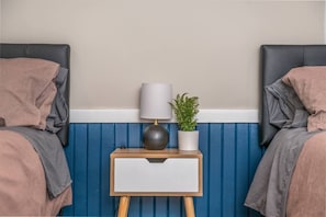 A bedroom with two beds, a bedside table with a lamp, a potted plant, and a white drawer unit. - Boho Home with driveway and lots of ensuite baths! (Atlanta)