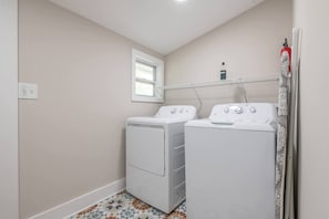 A laundry room with two white front-loading washers and dryers, a window, and a tiled floor. - Boho Home with driveway and lots of ensuite baths! (Atlanta)