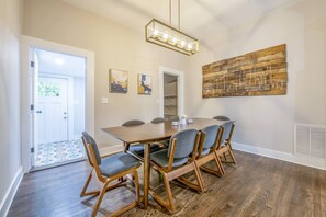 A dining area with a rectangular table, six chairs, a chandelier, and a large abstract painting on the wall.