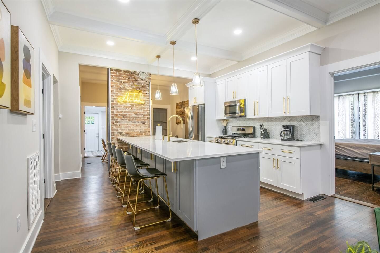 A modern kitchen with a central island, bar stools, a brick accent wall, and a large window.