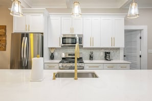 A modern kitchen with white cabinetry, stainless steel appliances, and gold fixtures.