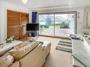 A living room with a sofa, a television, and a view of the outdoors through a sliding glass door. - Apartment Sleeps 2 With Parking, Pets Welcome (Penrith)