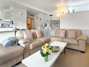 A modern living room with a beige sectional sofa, a white coffee table, and a vase of flowers. - Apartment Sleeps 2 With Parking, Pets Welcome (Penrith)