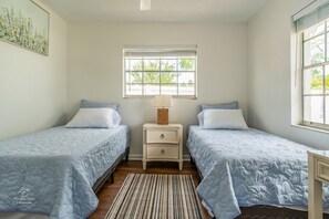 A bedroom with two beds, a nightstand, a lamp, and a window with a view of greenery. - Relaxing 3-Bedroom Vacation Home (Spring Hill)