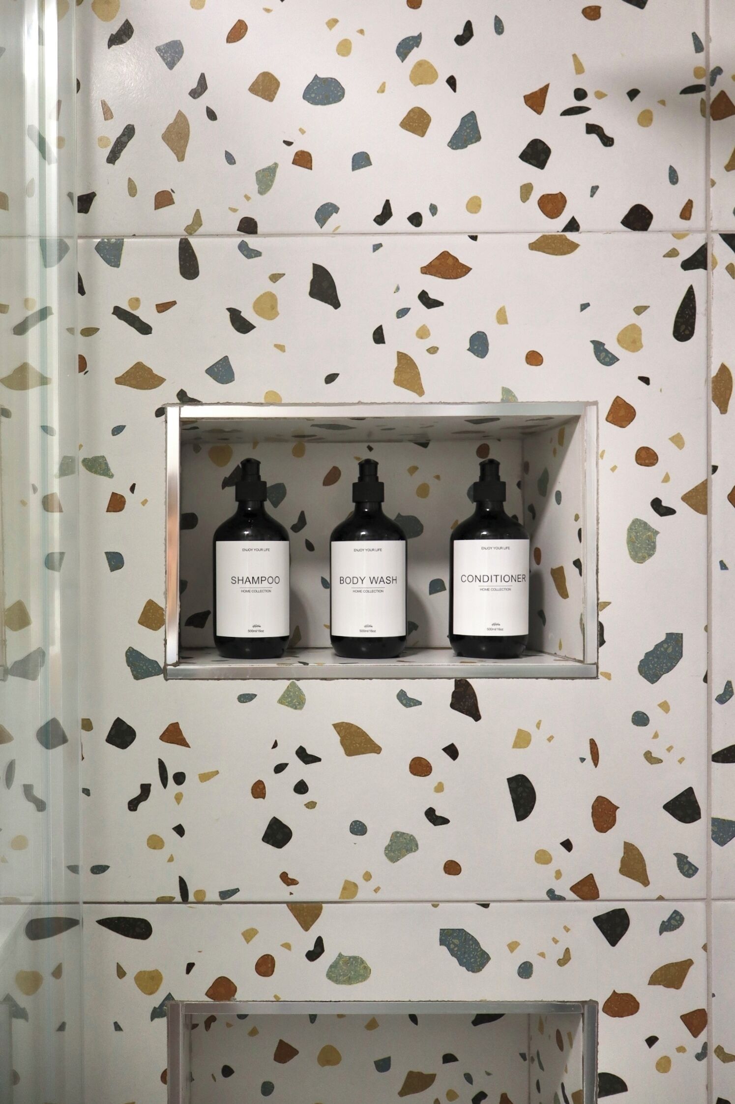 A bathroom with a terrazzo floor pattern and a shelf containing three bottles of personal care products.