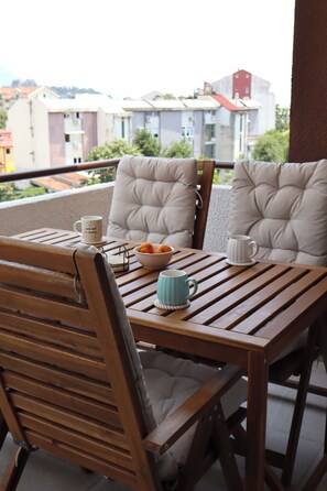 Mesa de madeira com duas cadeiras estofadas numa varanda com vista para a cidade.