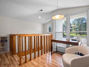 Ein Zimmer mit einem Holztisch, einem weißen Stuhl und Blick ins Freie durch große Fenster.