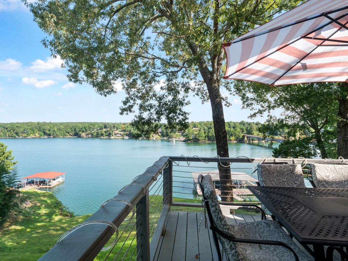 A lakeside deck with outdoor furniture, a view of the lake, and a distant shoreline.