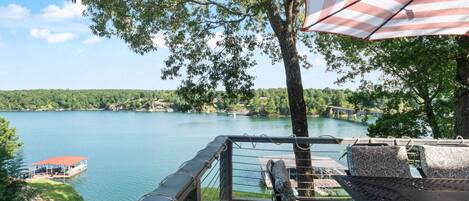 A lakeside deck with outdoor furniture, a view of the lake, and a distant shoreline.