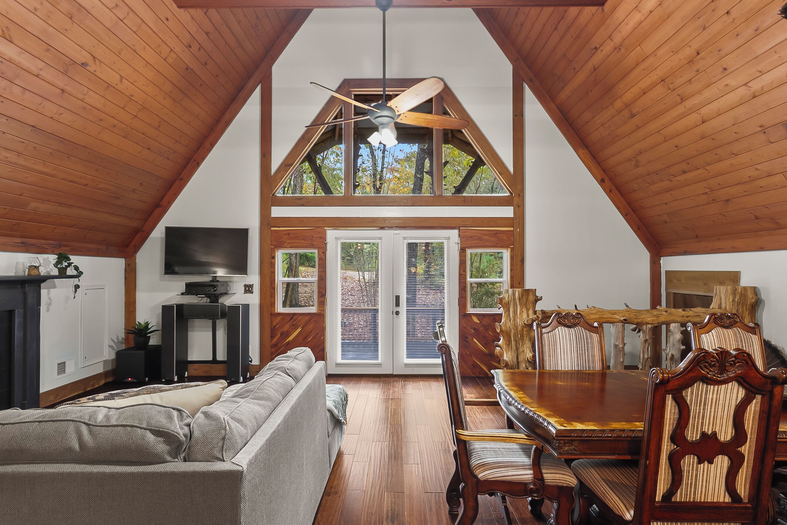 Un loft spacieux avec de hauts plafonds, des poutres apparentes, un coin repas avec une table et des chaises en bois, un canapé et un téléviseur.