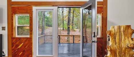 A wooden interior with a large glass door leading to a deck, surrounded by trees.