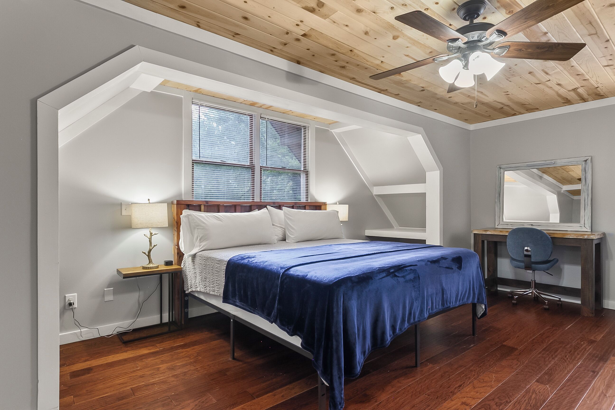 Une chambre à coucher comprenant un lit, un bureau, une chaise, un ventilateur de plafond et une fenêtre avec des stores.