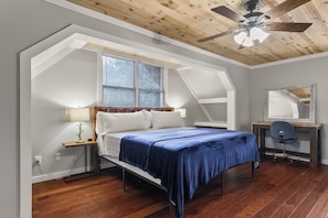 A bedroom with a bed, a desk, a chair, a ceiling fan, and a window with blinds.