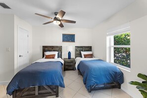 A bedroom with two beds, a ceiling fan, a nightstand, and a window with a view of greenery. - Delightful 3-bedroom house in Key Colony Beach with Inch Beach Access & Dockage (Key Colony Beach)