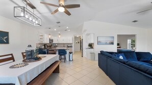 Eine moderne Küche mit weißen Schränken, ein Essbereich mit Holztisch und -stühlen sowie ein blaues Sofa im Wohnzimmer.