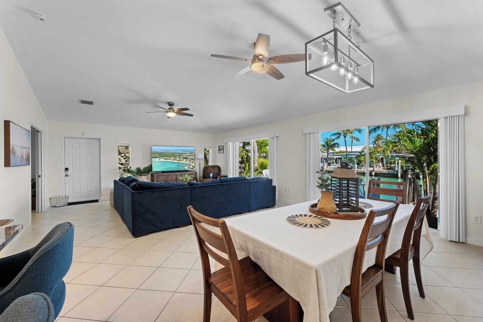 A spacious living area with a large sofa, a dining table with chairs, a ceiling fan, and a view of a pool through large windows.