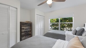 Ein Schlafzimmer mit zwei Betten, einem Deckenventilator, einem Kleiderschrank und einem Fenster mit Blick auf Grünflächen.