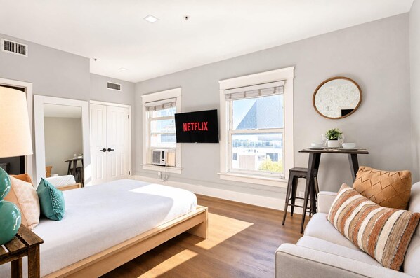 A modern bedroom with a bed, a TV, a desk, and a couch. - The Penn Hotel - Queen Bed, AC & Gaslamp Nightlife! (San Diego)
