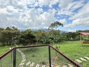 A fenced outdoor area with a paved path, surrounded by greenery and trees.