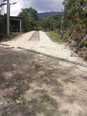 Een geplaveid pad dat leidt naar een gebouw met een metalen dak, omgeven door begroeiing en een glooiend landschap.