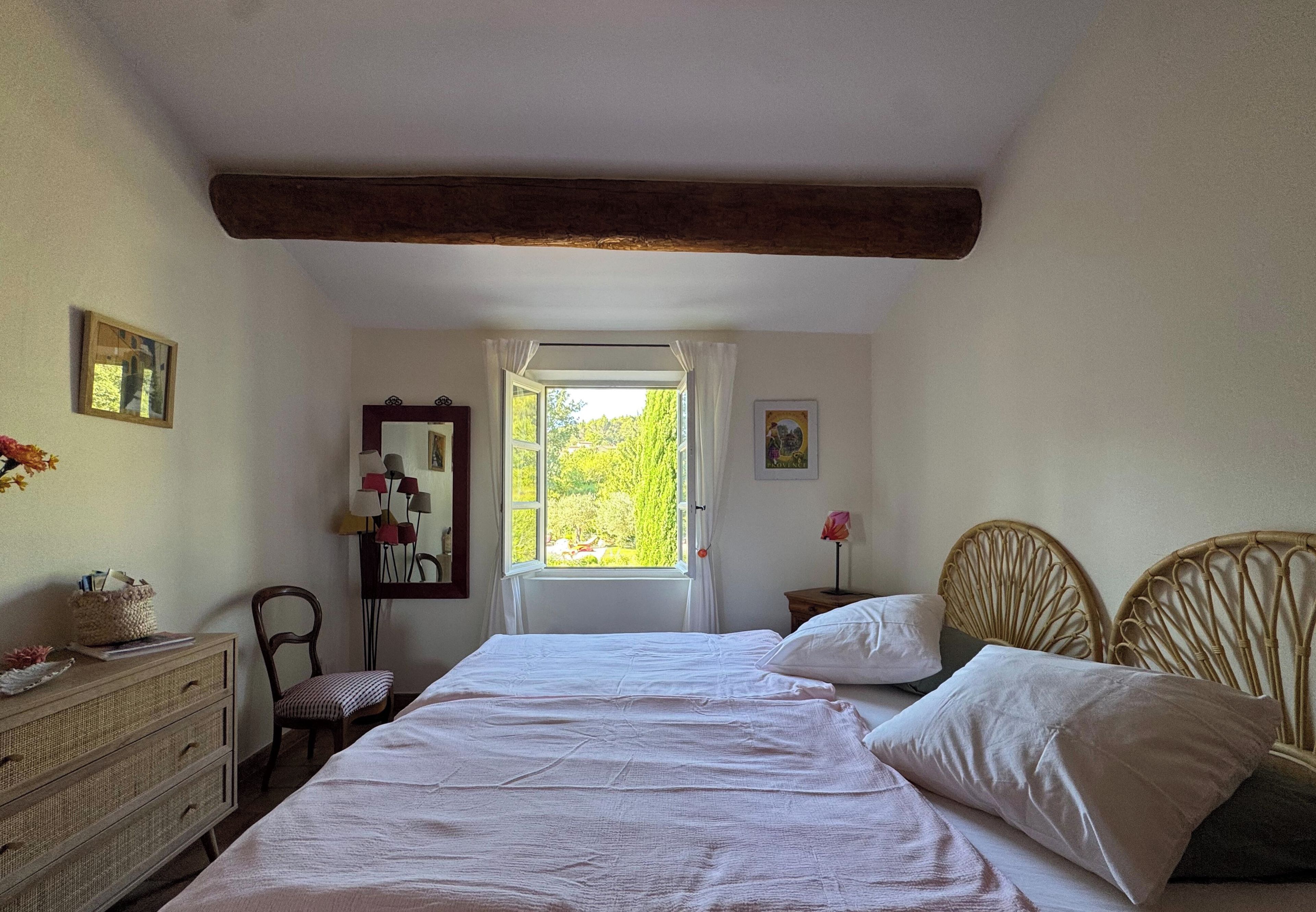 A bedroom with a large bed, a dresser, a chair, a mirror, and a window with a view of greenery.