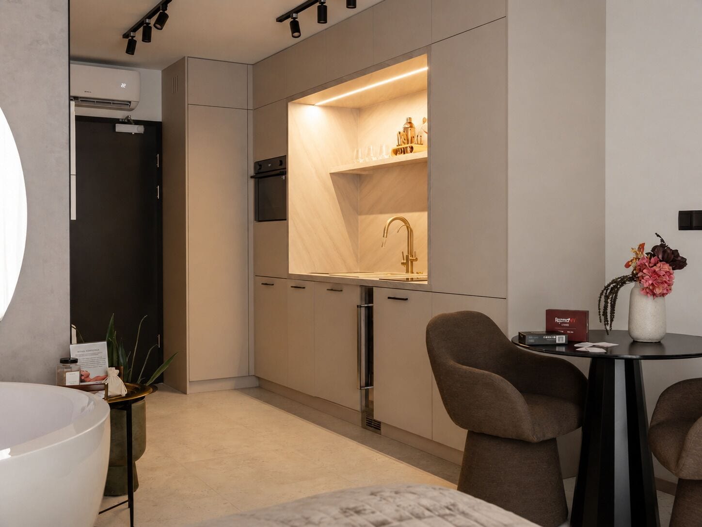 A modern kitchen with a built-in oven, a sink with a gold faucet, and a dining area with a round table and chairs.