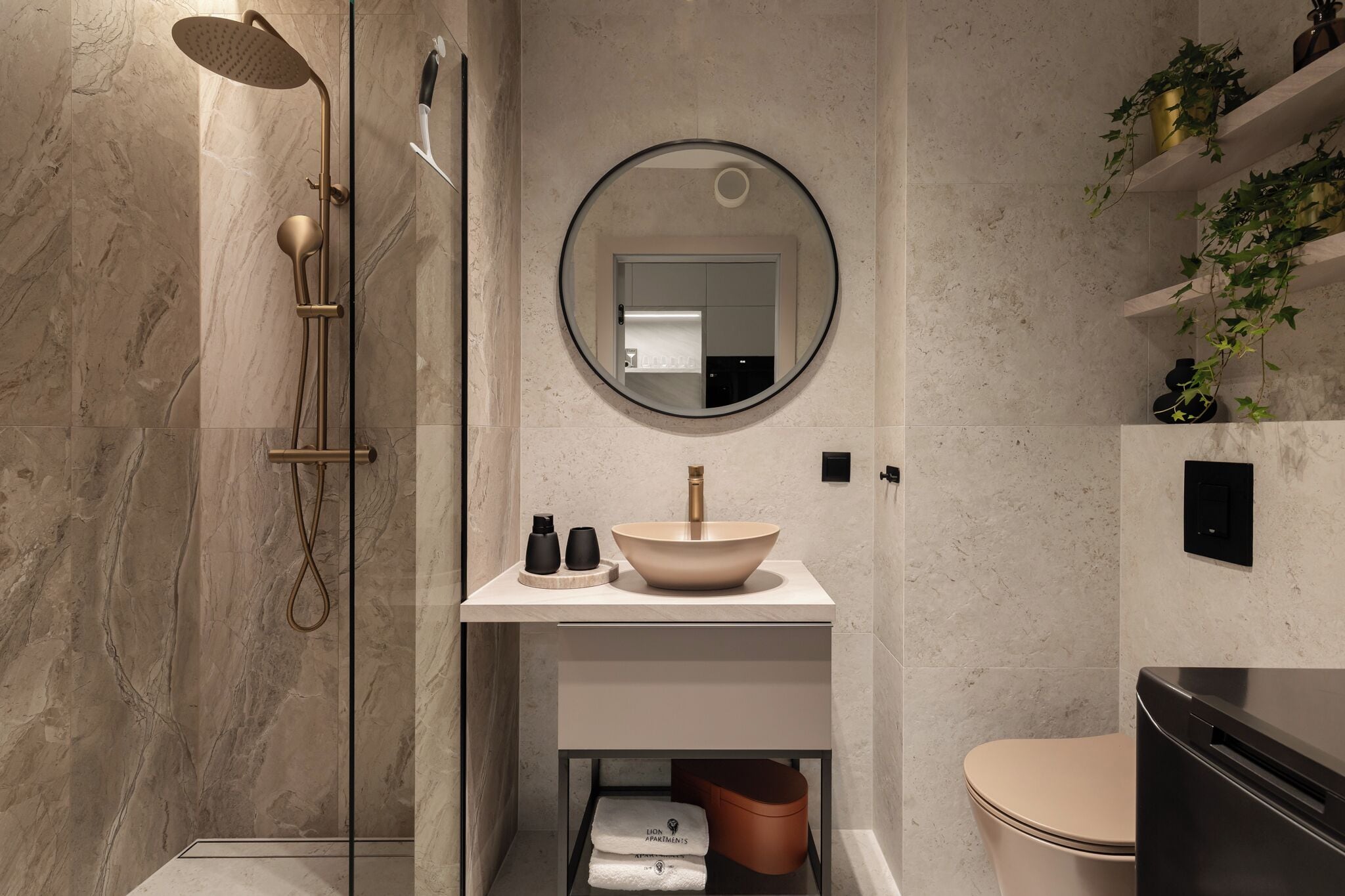 Ein modernes Badezimmer mit einer gläsernen Duschkabine, einem runden Spiegel, einem beigen Waschbecken und einer Toilette.