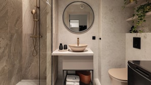 Une salle de bain moderne avec une douche à parois de verre, un miroir rond, un lavabo beige et des toilettes.