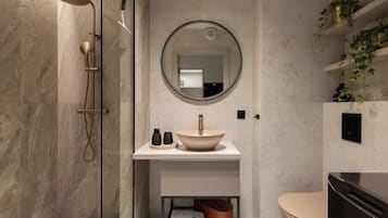 Ein modernes Badezimmer mit einer gläsernen Duschkabine, einem runden Spiegel, einem beigen Waschbecken und einer Toilette.