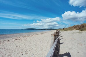 A sandy beach with a wooden fence leading to the water, under a clear sky. - Ty Pen (Pwllheli)