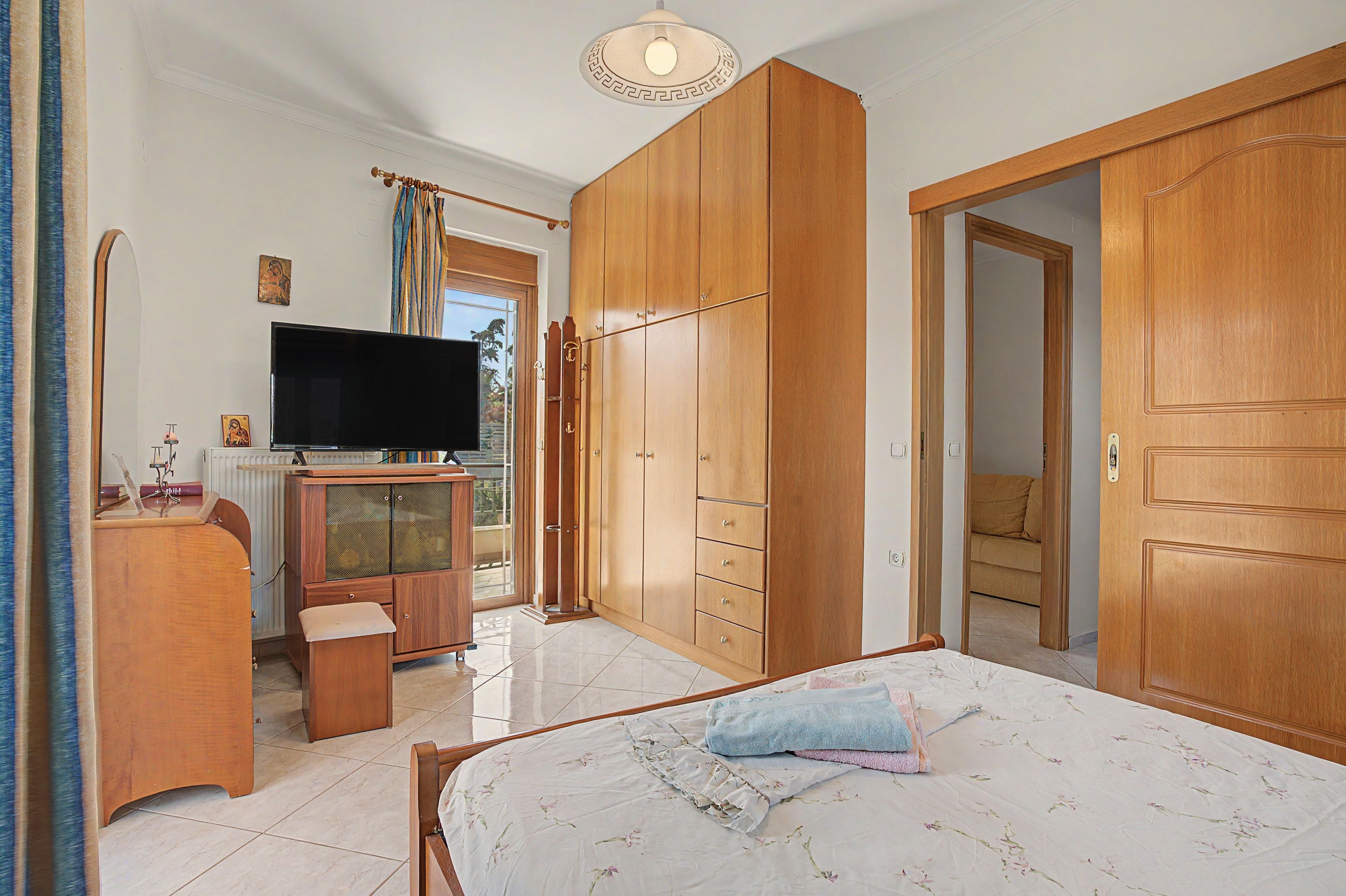 A bedroom with a bed, a television, wooden wardrobe, and a small desk.