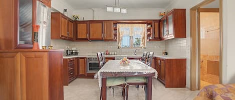 Una cocina con armarios de madera, una mesa de comedor y un ventanal con cortinas.